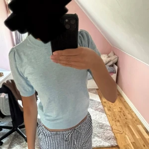Ljusblå stickad topp med puffärm - Supersöt ljusblå stickad topp med kort puffärm och rund hals. Sitter tajt men ändå bekvämt och har en clean, enkel look som passar perfekt till jeans eller kjol. Materialet är mjukt och stretchigt, vilket gör den skön att bära hela dagen.