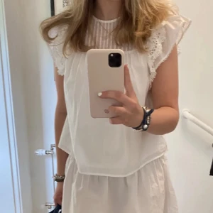 Vit blus med spets och volang - Superfin vit blus från &Other Stories med volangärmar och spetsdetaljer. Blusen har rund halsringning, tunna vertikala ränder upptill och är ärmlös med romantiska volanger längs axlarna. Perfekt för en fräsch och somrig look!