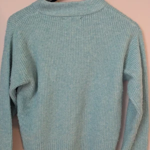 Ljusblå stickad tröja från Zara - Mysig ljusblå stickad tröja från Zara med ribbad krage och muddar. Tröjan har en enkel, klassisk design med långärmade ärmar och är perfekt för kyliga dagar. Materialet är mjukt och ger en skön känsla mot huden.