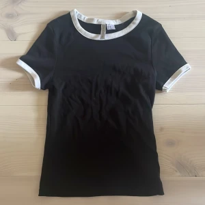 Svart t-shirt med vita kanter H&M Divided - Svart t-shirt från H&M Divided med vita ribbade kanter vid halsringning och ärmslut.