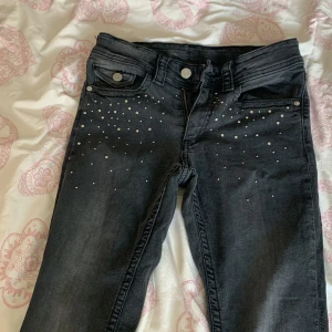  Låg midja det svarta jeans med nitar  - Snygga svarta jeans med raka ben och coola silvriga nitar framtill och på bakfickorna. Klassisk femficksmodell med knapp och dragkedja. Perfekta för dig som vill ha lite extra edge i din outfit.