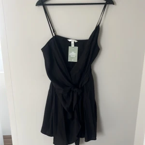Svart omlottklänning från H&M - Snygg svart omlottklänning i storlek M från H&M med smala axelband och knyt i midjan.