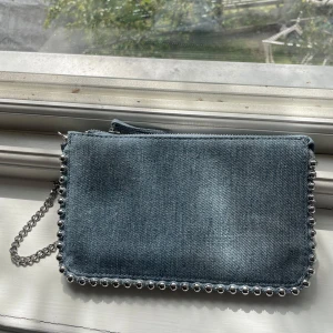 Jeans axelväska med silverkedja - Snygg axelväska i ljusblå jeans med coola silverfärgade nitar runt kanterna och en kedja som axelrem. Väskan har dragkedja upptill och en clean, rektangulär form. Perfekt för dig som gillar denim och vill ha en unik detalj till outfiten. Skriv om du undrar något💞