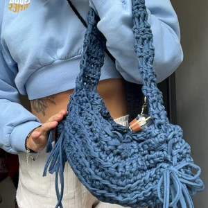 Virkad väska gjord av mig 🪼 - Säljer en handgjord blå axelväska i grovt stickat material. Väskan har en rundad form, bred axelrem och coola fransdetaljer på sidorna. Perfekt för dig som vill ha en unik accessoar som sticker ut.