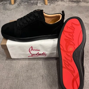 Christian Louboutin svarta skor - Svarta skor från Christian Louboutin i mocka med klassisk röd sula och diskret logga på sidan. Skorna har rund tå, svarta skosnören och en lyxig känsla med beige innersida. Perfekta för dig som vill sticka ut med exklusiv stil.