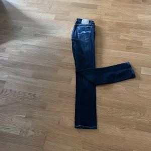 Mörkblå jeans från Nudie Jeans - Snygga mörkblå jeans från Nudie Jeans med kontrastsömmar och klassisk femficksdesign. Jeansen har raka ben och tydliga slitningar för en cool look. Tillverkade i bomull med dragkedja och detaljerad bakficka med vågig söm.