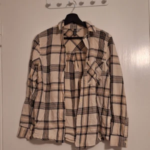 Beige och svart rutig skjorta H&M - Rutig skjorta från H&M i beige och svart med inslag av brunt. Skjortan har klassisk krage, knäppning framtill och en bröstficka. Långärmad modell i mjuk bomull, perfekt att styla lager på lager.