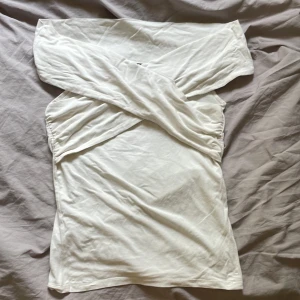 Vit omlott topp från Gina Tricot - Säljer en vit omlott topp från Gina Tricot i storlek M. Toppen har en snygg omlott-detalj över axlarna som ger en offshoulder-look. Tillverkad i mjuk bomull, perfekt för dig som gillar stilrena och trendiga plagg.