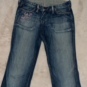 Blå jeans med rosa paljettdetalj - Snygga blå vintage jeans i bootcut. Dragkedjan har gått av & de är lite slitna vid benen. Annars i jättebra skick!! Skriv gärna vid ytterligare frågor!💘