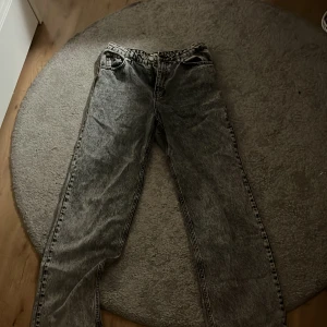 Acid wash jeans från NA-KD, strl 38 - Säljer ett par grå acid wash jeans från NA-KD i rak modell. Jeansen har klassisk femficksdesign, hög midja och cool tvätt som ger en retrovibe. Perfekta för dig som gillar en avslappnad men trendig look.