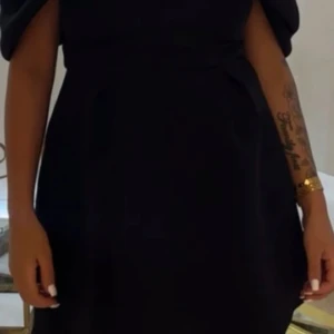 Svart kort klänning från ASOS DESIGN - Supersnygg svart kort klänning från ASOS DESIGN med dramatiska, voluminösa ärmar och markerad midja. Klänningen har en elegant och stilren look, perfekt för dig som vill sticka ut. Tillverkad i ett slätt material med dragkedja bak. Använd 1 gång 