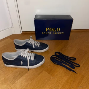 Mörkblå sneakers från Polo Ralph Lauren - Snygga mörkblå sneakers från Polo Ralph Lauren med vit broderad logga på sidan. Skorna har vita snören och vit sula. Klassisk och stilren design i syntetmaterial, perfekta till jeans eller shorts. Extra mörkblå skosnören medföljer.       Skorna har en lite sliten sula men är för övrigt i bra kvalitet. Säljes pga att de är för små.                                             Priset kan diskuteras.