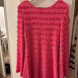 Rosa kortklänning med volangdetaljer - Säljer en superfin rosa kortklänning med lång ärm och coola volangdetaljer över hela klänningen.