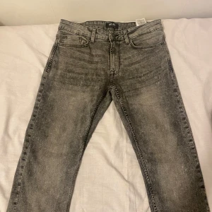 Grå jeans från Only & Sons - Snygga grå jeans från Only & Sons med tvättad look och klassisk femficksmodell. Jeansen har normal passform och raka ben, perfekt för en avslappnad stil. Tillverkade i mjukt jeanstyg med dragkedjegylf och bälteshällor.