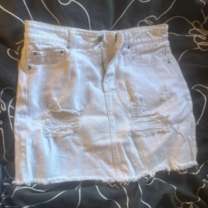 Vit jeanskjol från NLY Jeans - Snygg vit kort jeanskjol från NLY Jeans med slitna detaljer och rå kant nedtill. Kjolen har klassiska fickor fram och bak samt dragkedja och knapp i midjan. Perfekt för dig som gillar en cool och avslappnad stil.