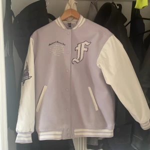 Ljuslila och vit bomberjacka - Säljer en ljuslila och vit bomberjacka från H&M med broderade detaljer. Jackan har tryckknappar och två öppna fickor framtill. Har lite fläckar som inte går bort i tvätten och några trådar som har börjat gå upp men inget man tänker jättemycket på. Perfekt hösten och skolstarten!!