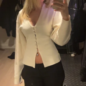 Krämvit v-ringad kofta med knappar - Säljer en fin tröja som inte kommit till användning. Den är i nyskick och passar perfekt till hösten! 