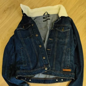 Blå jeansjacka med teddyfoder - Snygg blå jeansjacka från Only & Sons med vitt teddyfoder i kragen. Klassisk modell med knappar framtill, bröstfickor med lock och sidofickor. Perfekt för dig som vill ha en cool och tidlös look under höst och vinter.