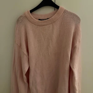 Ljusrosa stickad tröja från 157 - Mysig ljusrosa stickad tröja från 157 med rund hals och ribbade muddar. Tröjan har en enkel och clean design, perfekt för dig som gillar softa färger och oversized känsla. Passar dig som vill ha en chill och comfy look under höst och vinter.