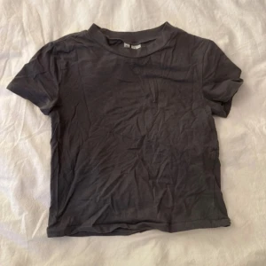 Mörkgrå basic t-shirt - En enkel och stilren mörkgrå t-shirt med rund hals och korta ärmar. Modellen är klassisk och passar dig som gillar en clean look. Materialet känns mjukt och skönt mot huden, perfekt till jeans eller shorts. T-shirten är enfärgad och har en normal passform.