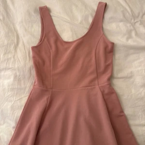 Rosa ärmlös kortklänning - Säljer en söt rosa klänning med rundad halsringning och ärmlös design. Kjolen är lätt utsvängd och ger en skön och ungdomlig vibe. Perfekt för dig som gillar enkel stil med lite extra färg. Materialet känns mjukt och stretchigt, vilket gör den bekväm att bära.