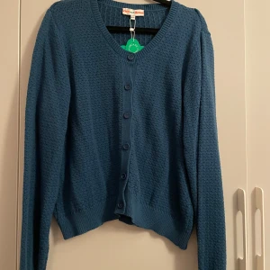 Blå kofta från Cissi och Selma XXL - Säljer en snygg blå kofta från Cissi och Selma i storlek XXL. Koftan är stickad i ekologisk bomull och har ett diskret strukturmönster, rundad hals och knappar framtill. Modellen heter Sigrid. Ny med prislappen kvar!