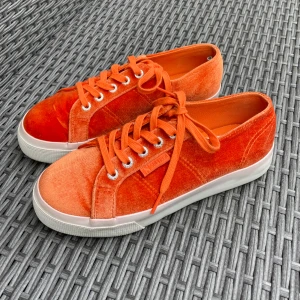 Orange sammetssneakers från Superga - Snygga sneakers från Superga i en riktigt poppig orange färg och mjuk sammet. Skorna har klassisk snörning, vit sula och rund tå. Perfekta för dig som vill sticka ut med färg och coolt material i vardagen. Sneakers med snörning i orange velvet sammet från Superga. Använda 1 gång så i mycket bra skick, vg se bilder. Storlek 37, normal i storlek.