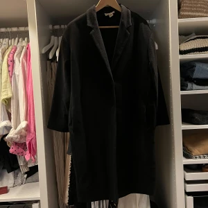 Svart kappa i ullmix - Stilren svart kappa med klassisk krage och dolda fickor. Rak och lite oversized passform, perfekt för lager-på-lager. Materialet är mjukt och känns lyxigt, troligtvis ullblandning. Enkel design som funkar till allt och ger en clean look. Den är använd och fickorna har slitage som syns på bild men inget jag har tänkt på stör mig vid daglig användning. Minns inte vad jag köpte den för men säljer för lågt pris för en ullblandningskappa.