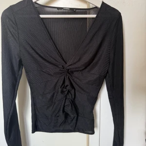 Svart ribbad långärmad topp Bik Bok - Svart långärmad topp från Bik Bok med djup v-ringning och snygg snörningsdetalj framtill. Toppen är ribbad och har en croppad passform som ger en trendig look. Tunt, lätt material som känns luftigt och passar perfekt till jeans eller kjol.