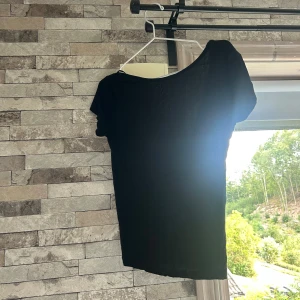 Svart basic topp med djup rygg - En svart, enkel topp med korta ärmar och djup, rundad rygg. Modellen är tight och har en klassisk, stilren look som funkar till allt. Tunt och mjukt material, perfekt för lager-på-lager eller som den är.