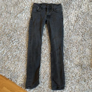 Svarta jeans från Nudie Jeans - Säljer ett par svarta skinny jeans från Nudie Jeans i storlek 32/34. Jeansen har klassisk femficksdesign, smal passform och är tillverkade i mjuk bomullsdenim. Perfekta för dig som gillar en clean och stilren look.