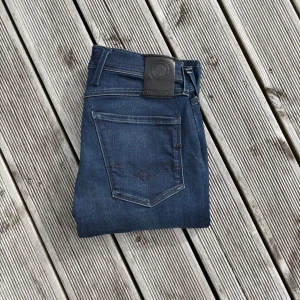 Replay Anbass slim fit jeans mörkblå  - Snygga Replay Anbass jeans i mörkblå tvätt med klassisk femficksdesign och raka ben. Jeansen har diskreta slitningar, svarta detaljer och logga på bakfickan samt svart Replay-läderpatch i midjan. Perfekta för dig som gillar stilrena jeans med modern passform. Kom gärna med frågor!🙌 W29 L30
