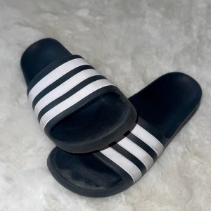 Adidas svarta sandaler med vita ränder - Säljer ett par klassiska Adidas sandaler i svart med de ikoniska tre vita ränderna över foten. 