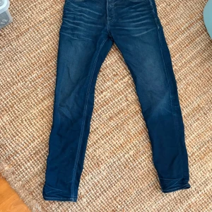 Mörkblå skinny jeans Jack & Jones - Snygga mörkblå skinny jeans från Jack & Jones i storlek 32/34. Jeansen har klassisk femficksdesign, diskreta slitningar och smal passform som sitter tajt längs benen. Perfekta för dig som gillar en modern och stilren look.