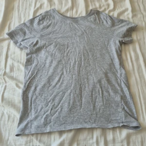 Grå t-shirt från Friboo - En enkel och mjuk grå t-shirt från Friboo med rund hals och korta ärmar. T-shirten är tillverkad i bomull och har en klassisk, normal passform. Perfekt för chill dagar och passar till allt. Snygg och basic stil som funkar året runt.