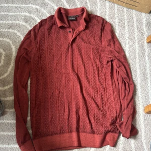 Vinröd pikétröja från Oscar Jacobson - Snygg vinröd pikétröja från Oscar Jacobson med kabelstickat mönster och klassisk krage med knappar. 100% ull, nypris: 2000