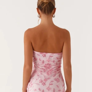 Rosa blommig axelbandslös kortklänning - Superfin axelbandslös kortklänning i ljusrosa med blommigt mönster och paljettdetaljer. Klänningen har en tight passform och är gjord i ett tunt, glansigt material med broderade blommor och pärlor. Perfekt för dig som vill sticka ut med en söt och feminin look.