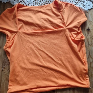 Orange kortärmad topp med fyrkantig ringning - Snygg orange topp med korta ärmar och fyrkantig ringning. Tillverkad i mjuk bomull, perfekt för varma dagar. Enkel och stilren design som är lätt att matcha med jeans eller kjol.