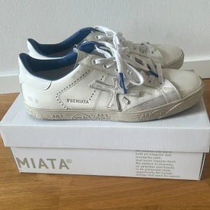 Vita sneakers från Premiata Steven - Snygga vita sneakers från Premiata Steven med coola detaljer på sulan och blå insida. Skorna är i skinn och har klassisk snörning samt rund tå. Perfekta för dig som gillar stilrena och trendiga sneakers med unik design. Köpta från farfetch, endast använda två gånger.