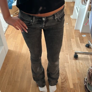 Svarta bootcut jeans låg midja - Säljer ett par svarta jeans med bootcut-modell och låg midja. Jeansen har klassisk femficksdesign och är i stretchigt denimtyg som sitter snyggt på kroppen. Perfekta för dig som gillar en tidlös look med lite edge.