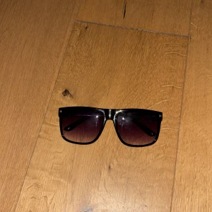 Helt nya Svarta solglasögon med rektangulära bågar - Helt nya Snygga svarta solglasögon med rektangulära bågar och mörka tonade glas. Klassisk och stilren design som passar till många olika outfits. Bågarna är i plast och har en modern känsla.