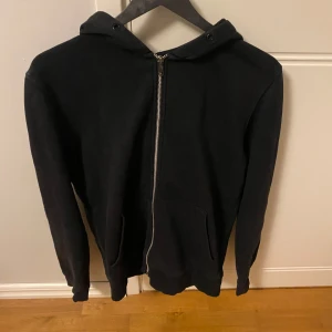 Svart zip hoodie från Jack & Jones - En klassisk svart hoodie från Jack & Jones med dragkedja framtill och luva . Tröjan har två fickor framtill och ger en stilren och snygg stil till sommaren, ganska bra skick 