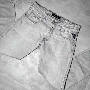 Ljusgrå jeansbyxor från Replay Anbass - Säljer ett par ljusgrå Replay Anbass jeans med klassisk femficksdesign och raka ben. Byxorna har dragkedjegylf och diskreta Replay-detaljer på fickorna. Perfekta för dig som gillar stilrena och bekväma jeans.
