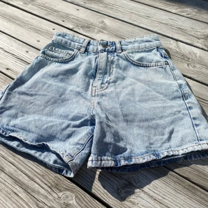 Ljusblå jeansshorts - Klassiska ljusblå jeansshorts med normal passform och fem fickor. De har bälteshällor och knappgylf. Perfekta för varma dagar och enkla att matcha med olika toppar.