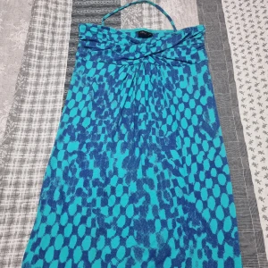 Turkos och blå mönstrad klänning från Lindex - Säljer en turkos och blå klänning från Lindex med halterneck och grafiskt mönster. Klänningen har en snygg drapering framtill och är ärmlös. Perfekt för varma dagar och somriga tillfällen.