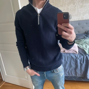 Mörkblå halvzip tröja från Kronstadt - Säljer en mörkblå stickad tröja från Kronstadt med halv dragkedja och hög krage. Tröjan har lång ärm och ribbade muddar, perfekt för en stilren och avslappnad look. Sjukt skön overshirt! 