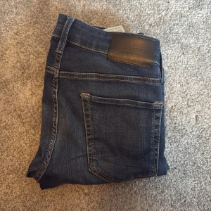 Mörkblå slim jeans från Jack & Jones - Snygga mörkblå jeans från Jack & Jones i modellen Slim/Glenn. Jeansen har klassisk femficksdesign, dragkedja och knapp framtill samt diskreta slitningar för en modern look. Perfekta för dig som gillar en smal passform.