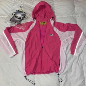 Corteiz - Säljer en snygg rosa och vit vindjacka från Corteiz med en skön luva och reflekterande detaljer⚡️. Perfekt för dig som vill sticka ut med streetwear och cool design.🚨🚨🚨 SNABB AFFÄR= BÄTTRE PRIS