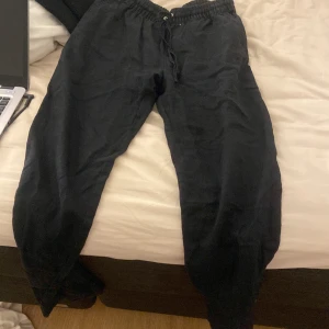 Svarta linnebyxor med snören - Svarta linnebyxor med elastisk midja och snörning. Byxorna har en loose passform och är tillverkade i ett mjukt material, perfekta för chill dagar fast man ändå vill va lite snygg. Snygg och enkel design utan mönster.