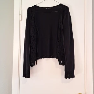 Svart kofta med virkade detaljer Ze-Ze - Svart kofta från Ze-Ze i storlek S. Koftan har snygga virkade detaljer längs kanterna och vid ärmsluten samt knytning framtill. Långärmad och i mjukt stickat material, perfekt för lager-på-lager och en chill look. Använd men i bra skick. Saknar en sån liten metallögla(se bild) men jag alltid haft bara stängt med snör så inte störd mig. 
